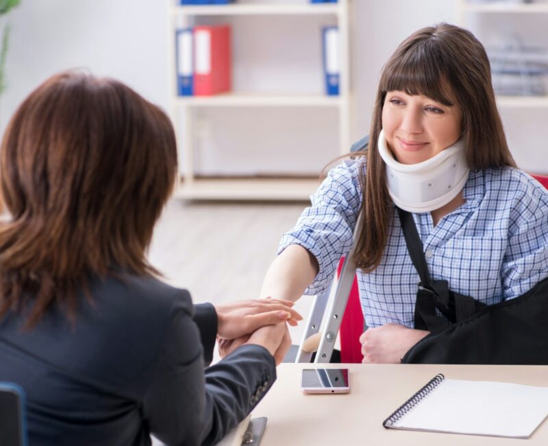 Car accident lawyer meeting with injured client wearing neck brace and arm sling during legal consultation